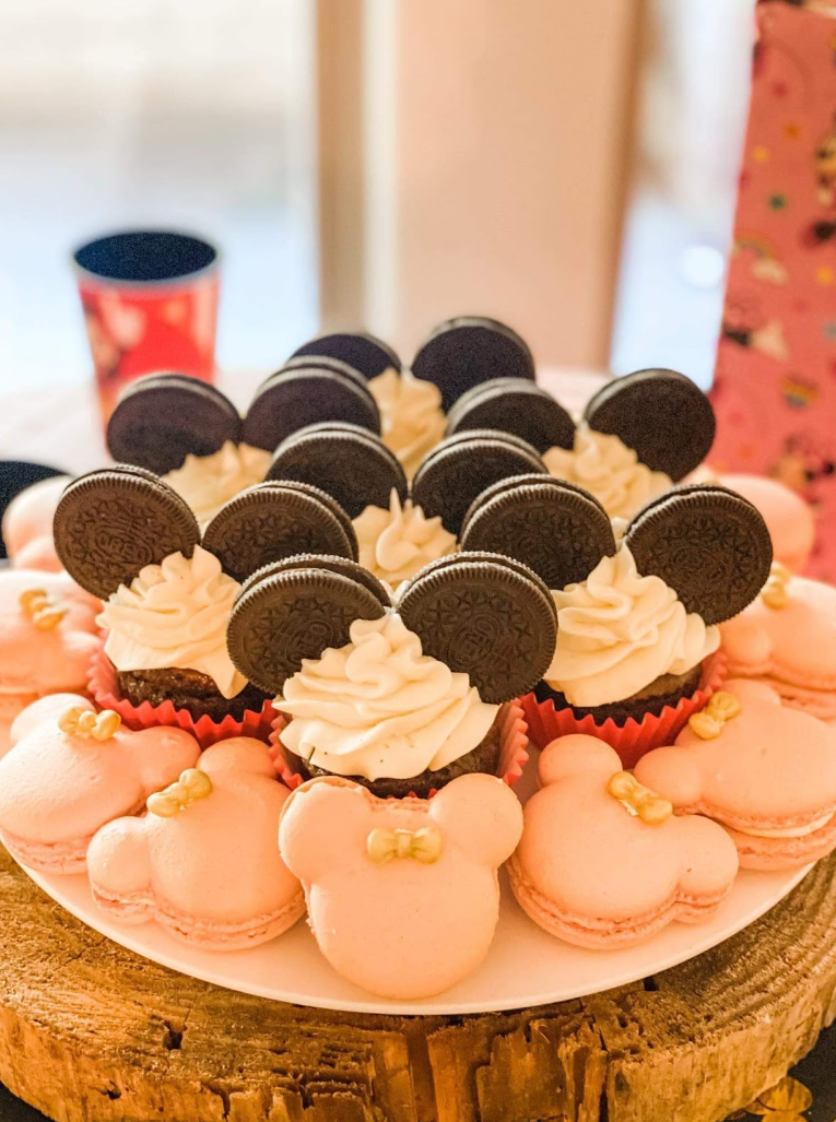A plate of Minnie Mouse-shaped macarons and cupcakes topped with icing and Oreos cookies