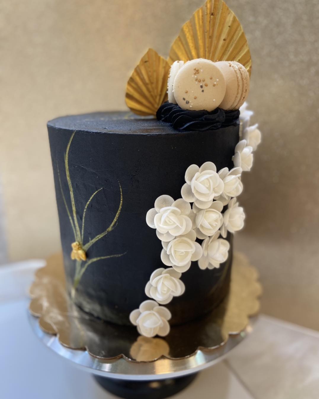 A black cake decorated with white flowers and macarons